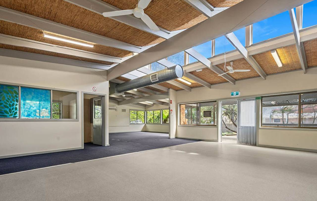Large open room with raked ceiling, exposed beams, clerestory glazing and carpet to one half.